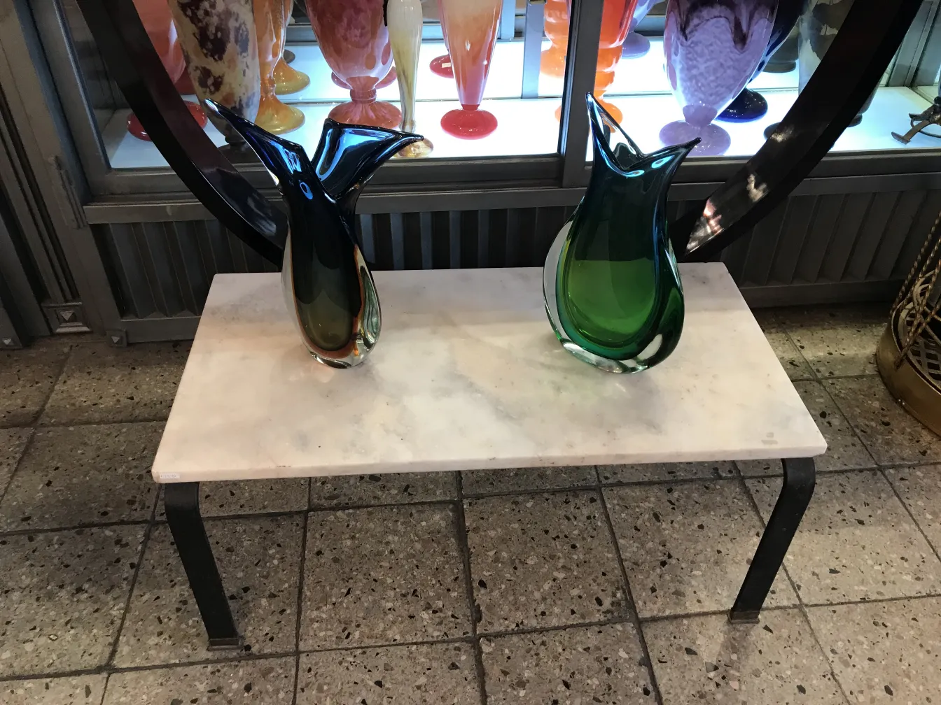 vaso de murano antigo, verde e preto, em mesa de mármore, com outros vasos ao fundo