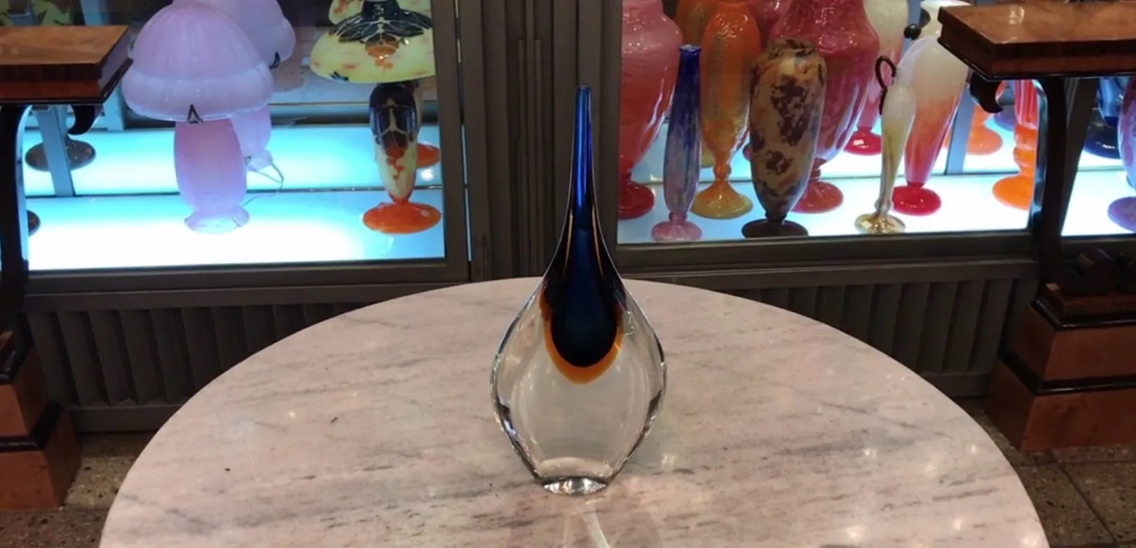 Vase Murano stylisé avec des couleurs vives sur une table en marbre près d'autres objets décoratifs.