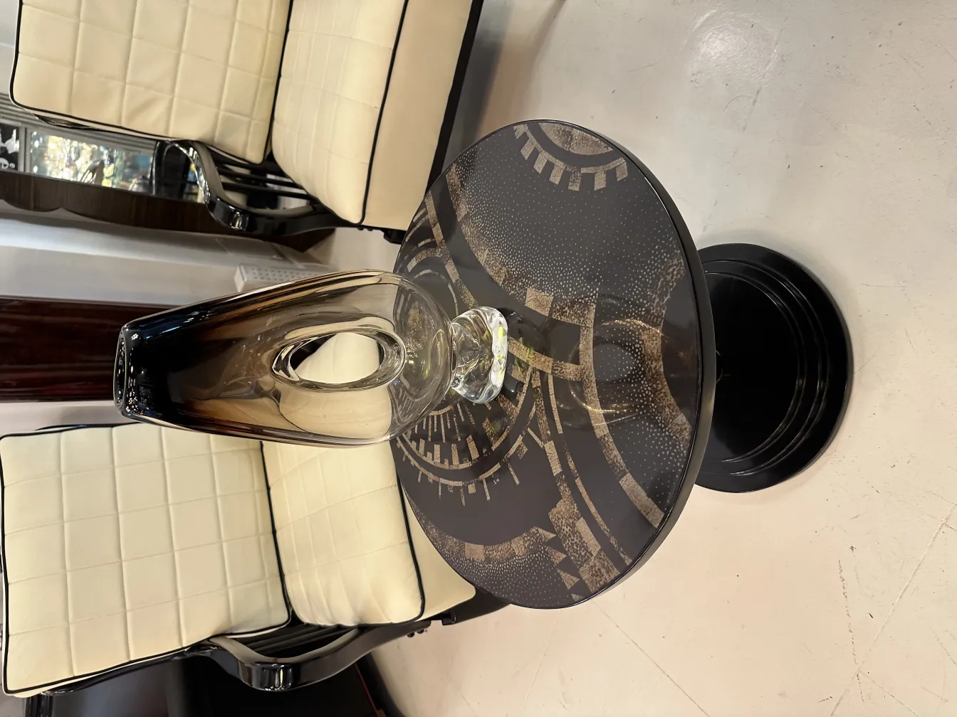 Vaso de Murano antigo com uma forma elegante e estilo clássico, colocado sobre uma mesa preta com fundo decorativo. Cadeiras ao redor.