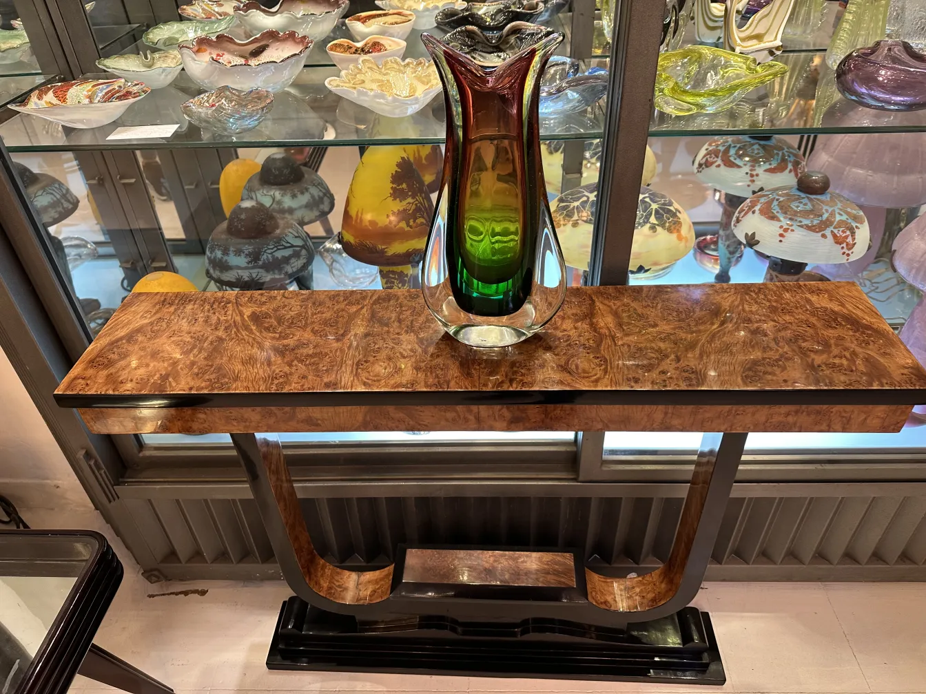 antike Murano-Vase in verschiedenen Farben auf elegantem Tisch mit dekorativen Objekten im Hintergrund.