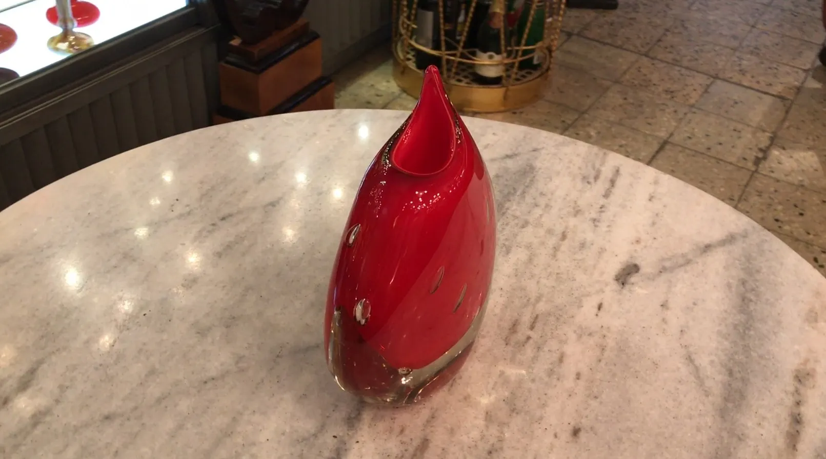 vase rosso di murano con forma curva su tavolo di marmo, sfondo con oggetti decorativi