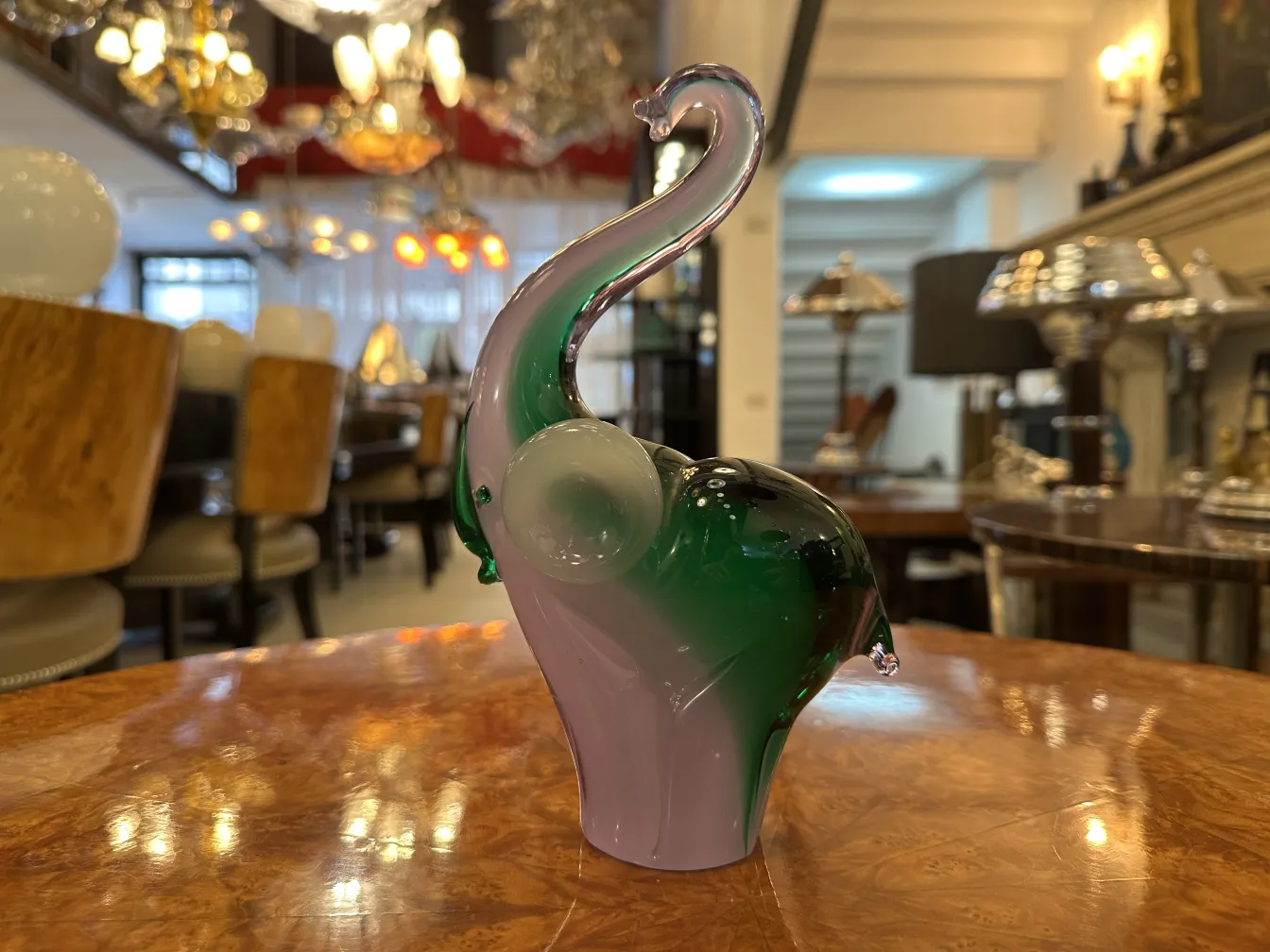 glas-elefant mit grünen und lila details vor antikem möbelhintergrund