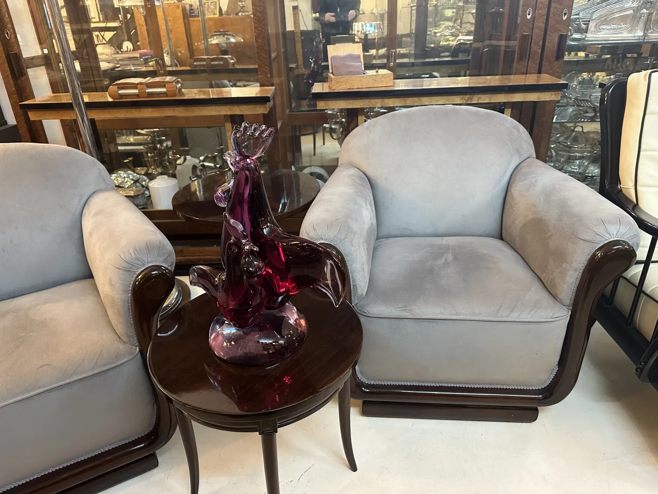 Escultura de Murano em tons roxos sobre uma mesa redonda, em um ambiente vintage com poltronas