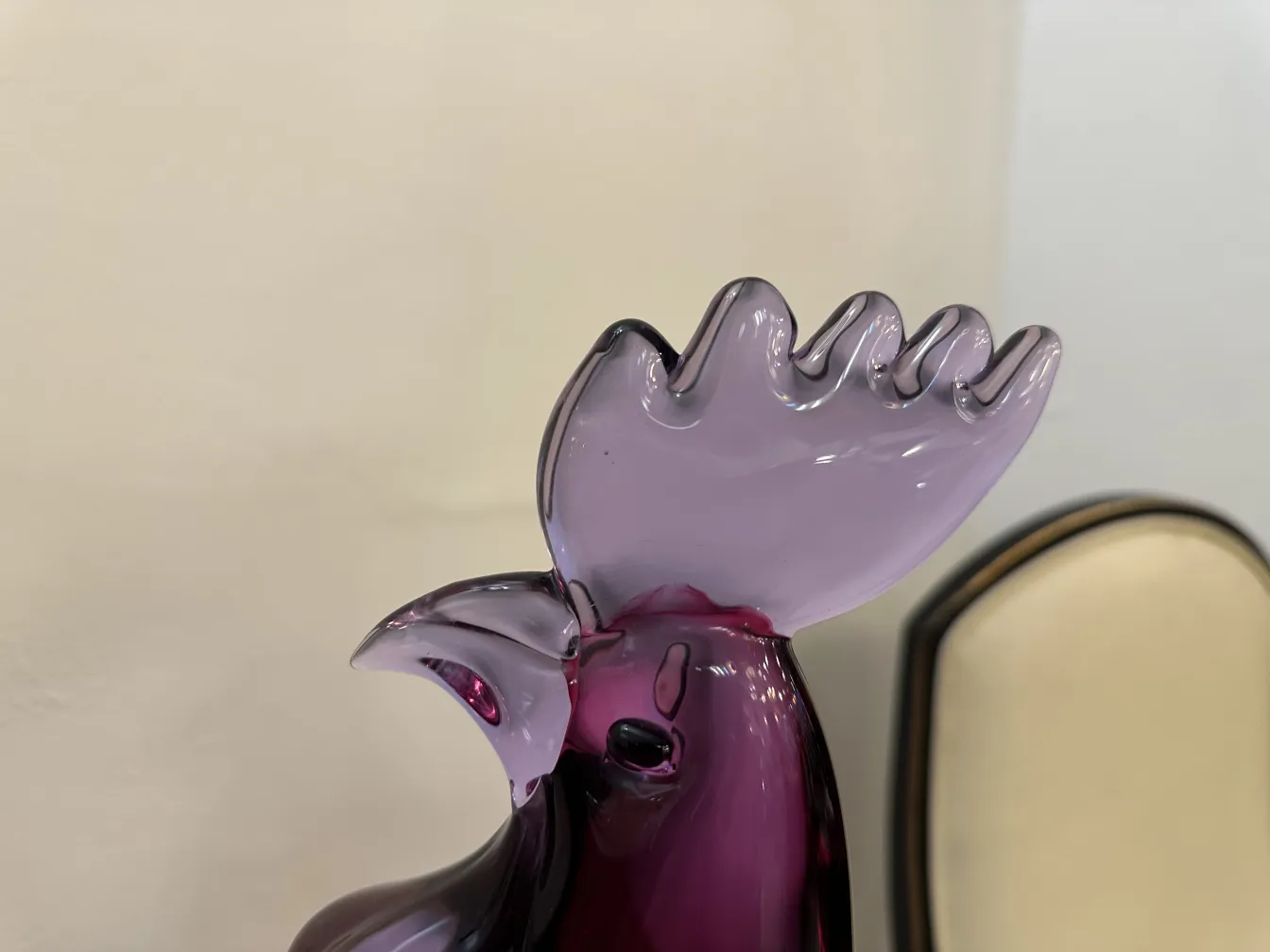 Dettagli di una scultura di murano a forma di gallo, colori viola e nero, sfondo chiaro.