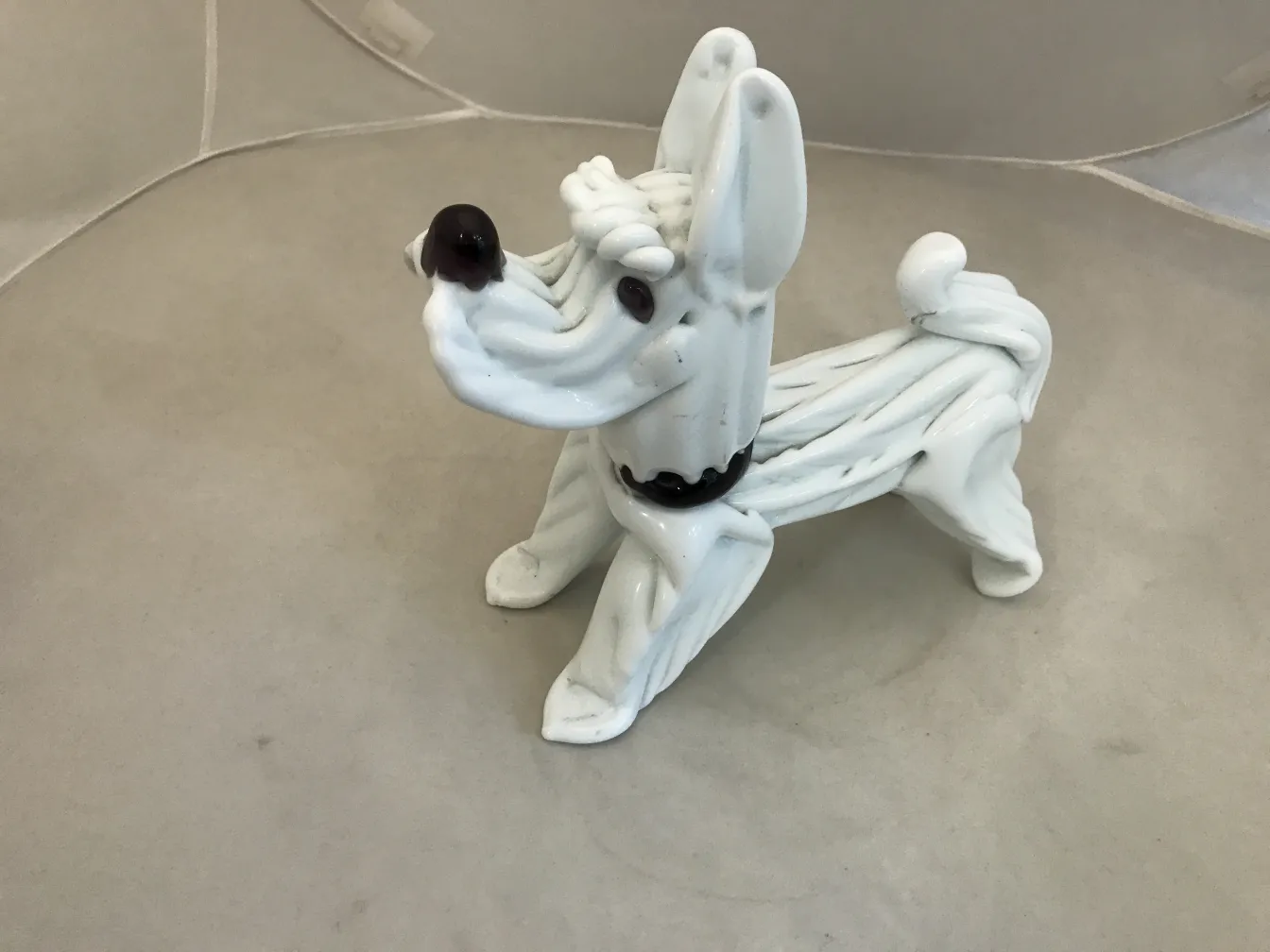 escultura de murano de un perro blanco con detalles oscuros en un fondo neutro