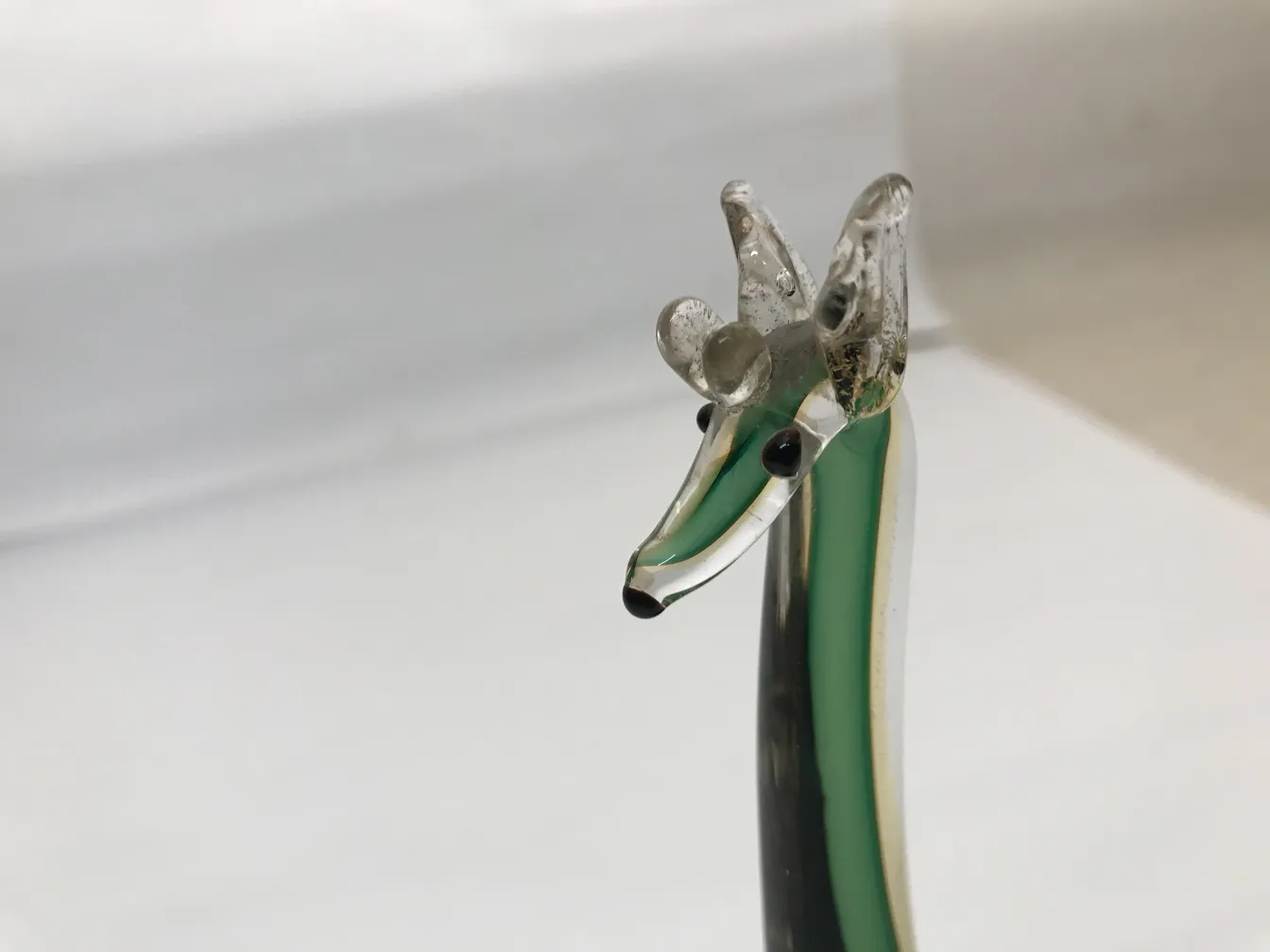 고대 무라노 동물 조각, 녹색 톤과 검은색 디테일이 있는, 흰색 배경에서 돋보입니다.