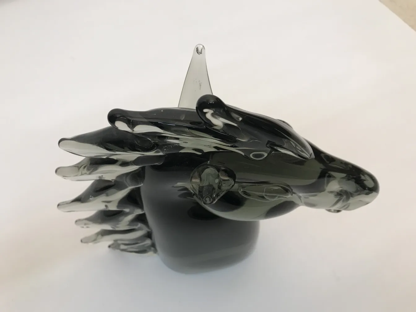 Antike Murano-Skulptur, die ein Tier darstellt, mit fließenden Formen und dunklen Farben. Neutraler Hintergrund.