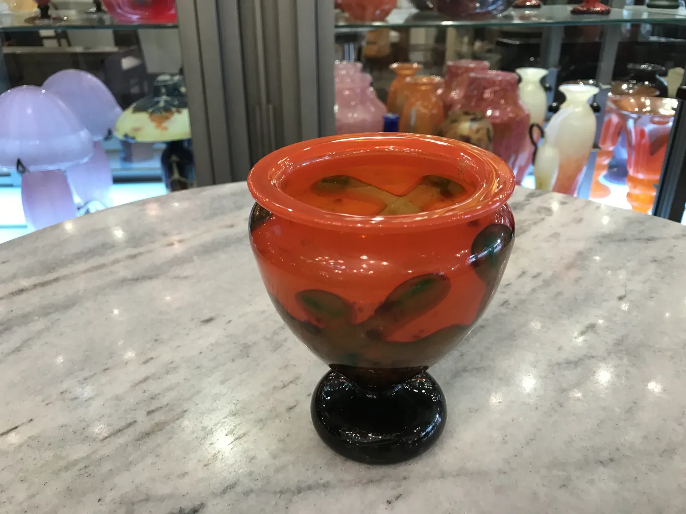 Verre signé de forme ronde en tons orange et noir, entouré d'antiquités.