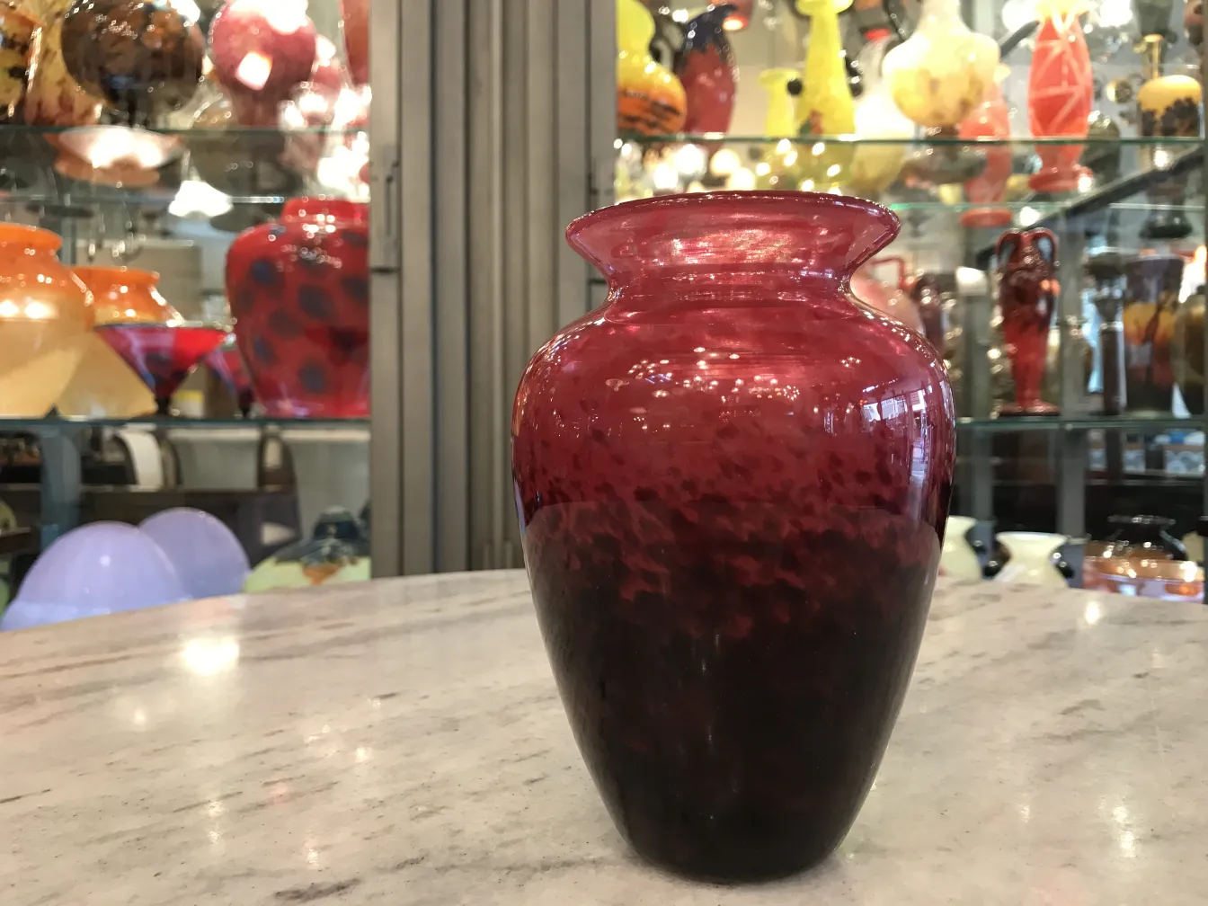 roter glas vase mit unterschrift, dunkler grund, umgeben von anderen glasobjekten