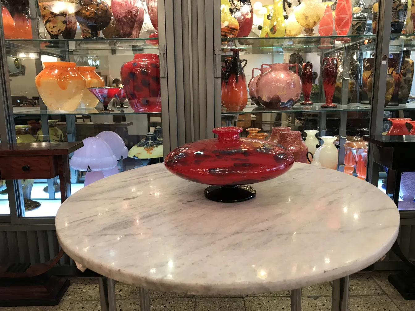 Verre antique signé par Schneider en rouge brillant, exposé parmi d'autres objets en verre.