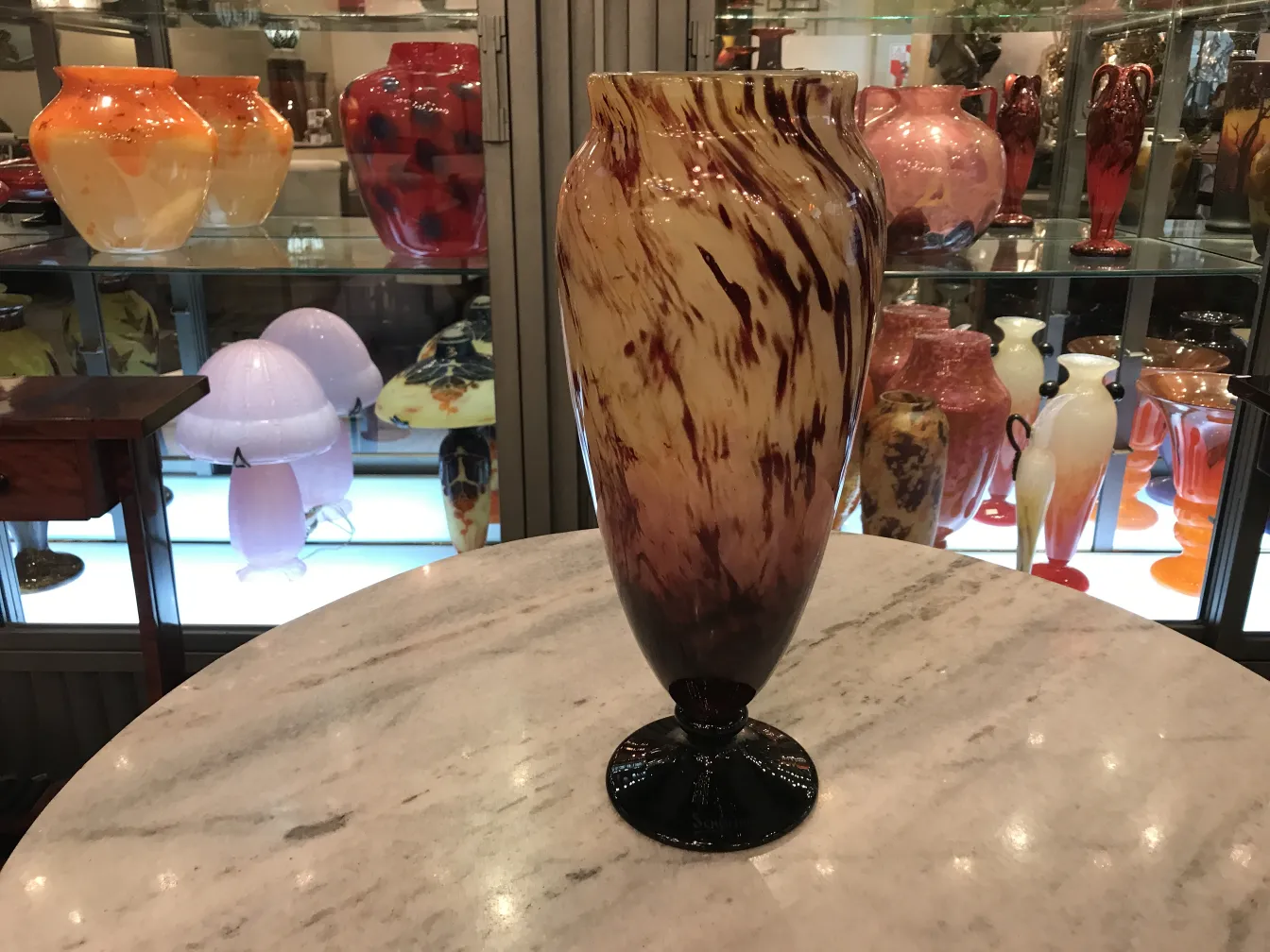 elegante antike vase mit braunen und beigen tönen, signiert, im hintergrund mit bunten glasobjekten.