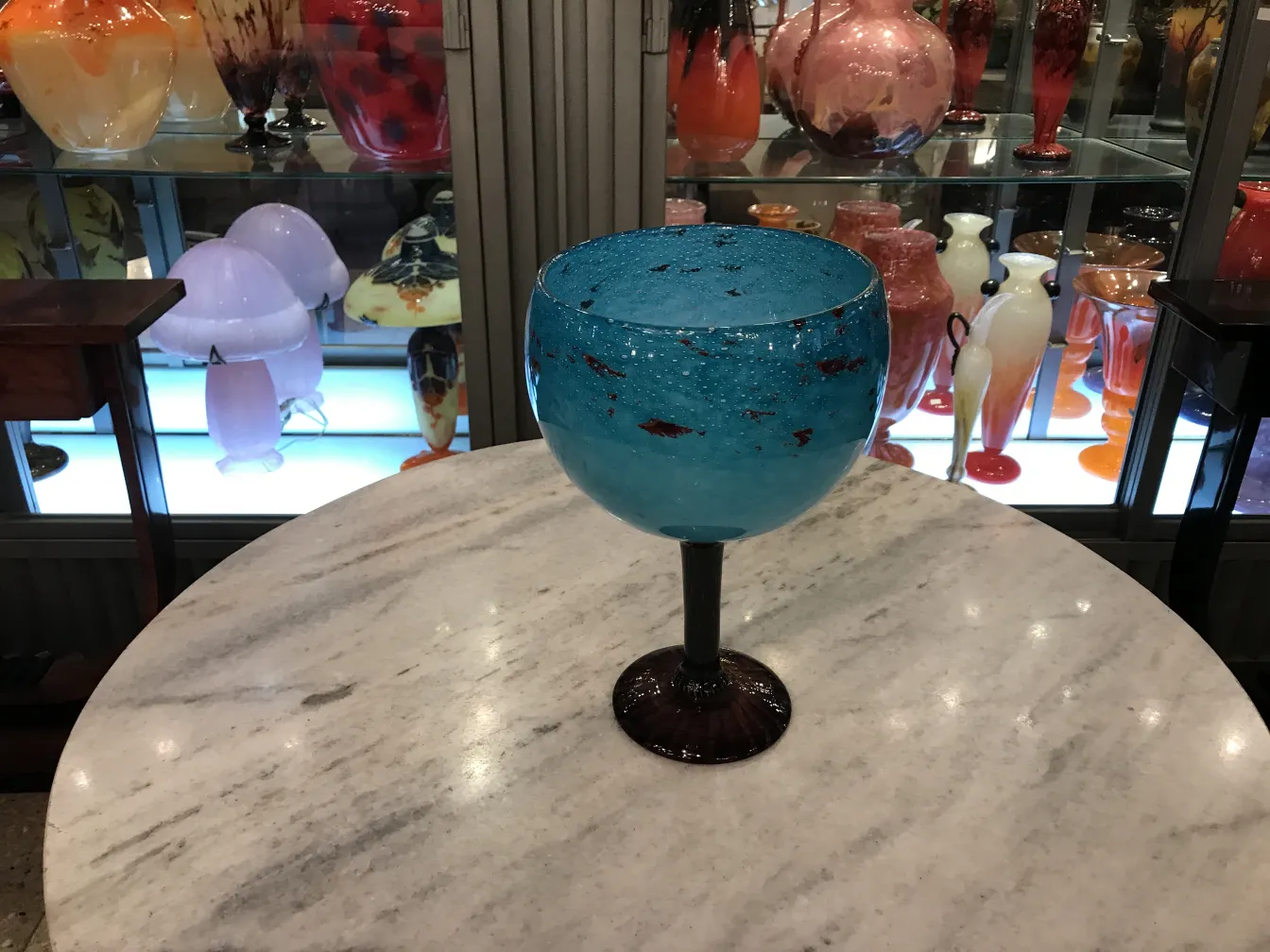 Antikes signiertes Glas von Schneider, leuchtend blaue Farbe auf einem Marmortisch, Hintergrund mit verschiedenen Antiquitäten.