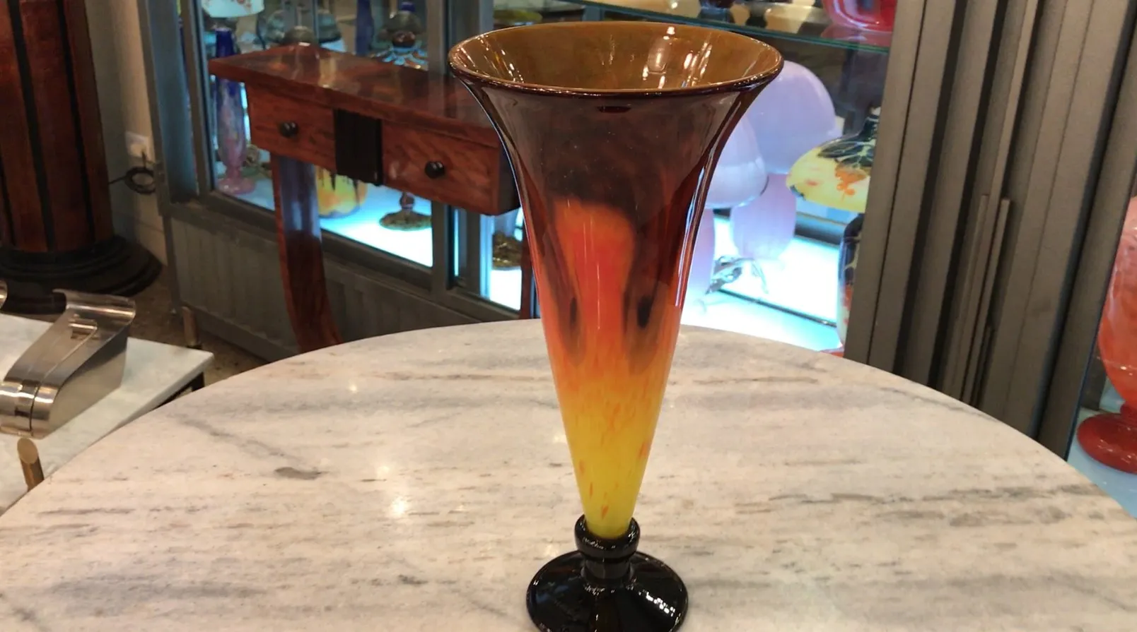 Vase en verre signé Schneider, avec un design décoratif aux couleurs chaudes, posé sur une table.