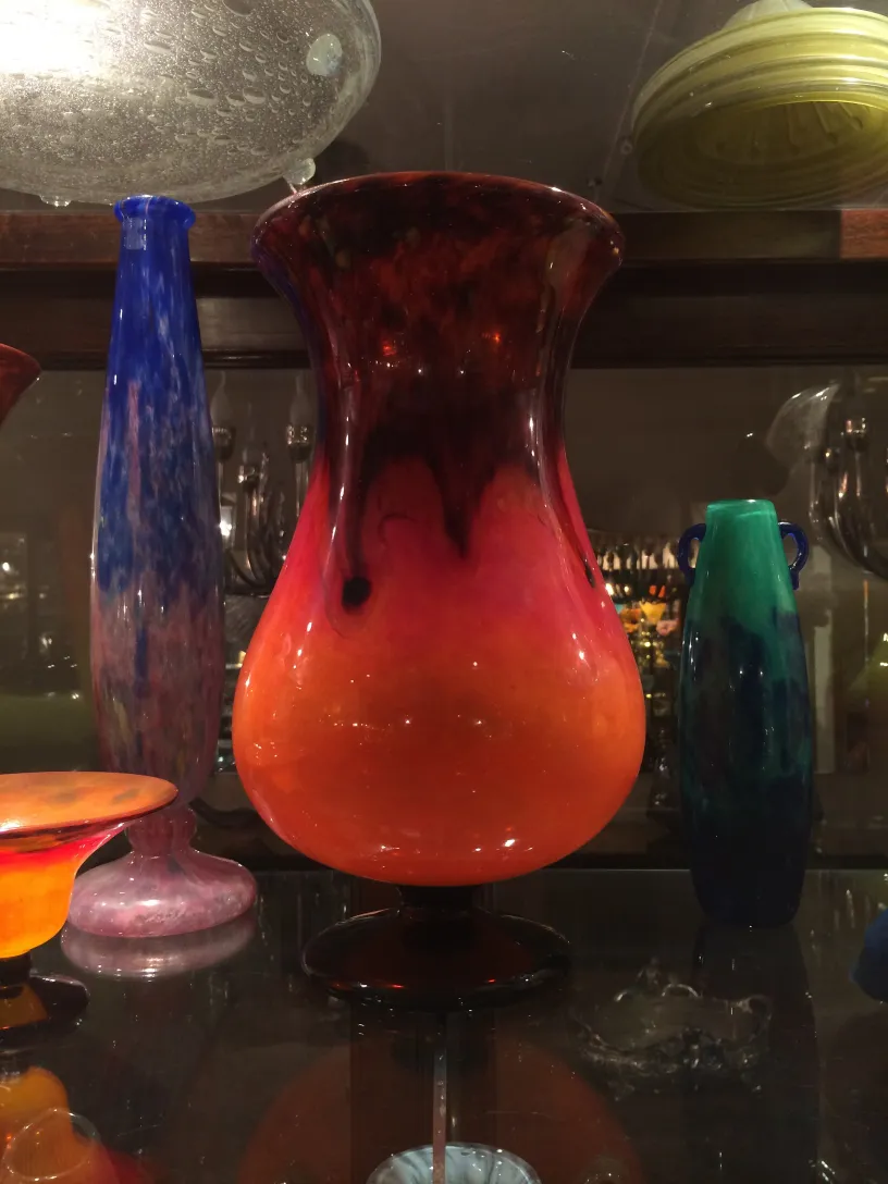 un vaso in vetro firmato con un gradiente vibrante di toni caldi, circondato da altre antichità