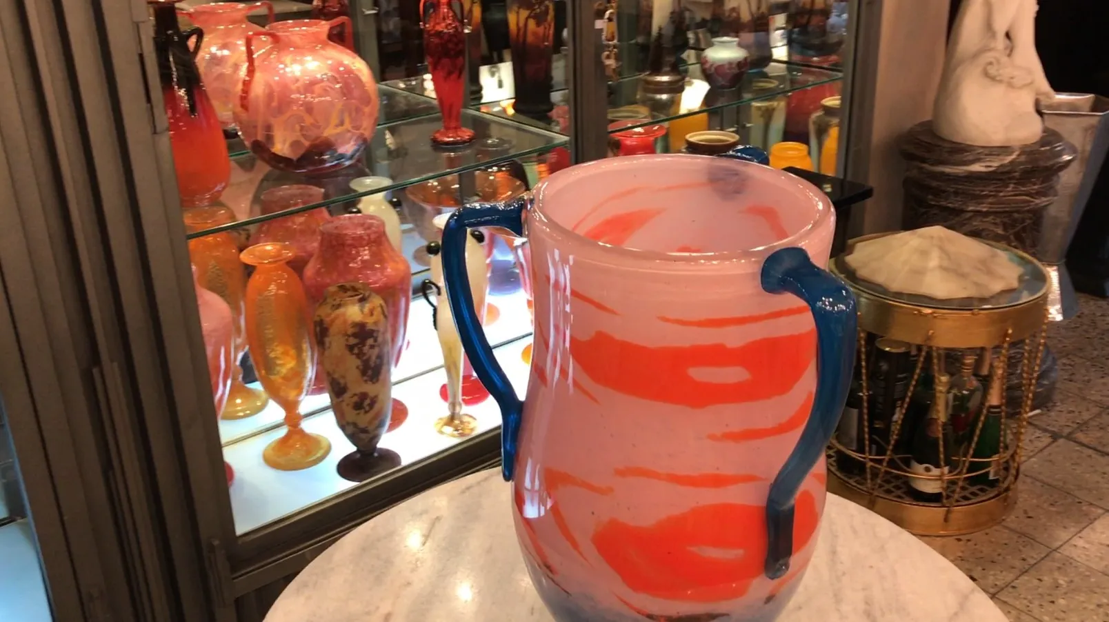 Jarra de vidrio con diseño en tonos rosa y azul, ambiente antiguo.