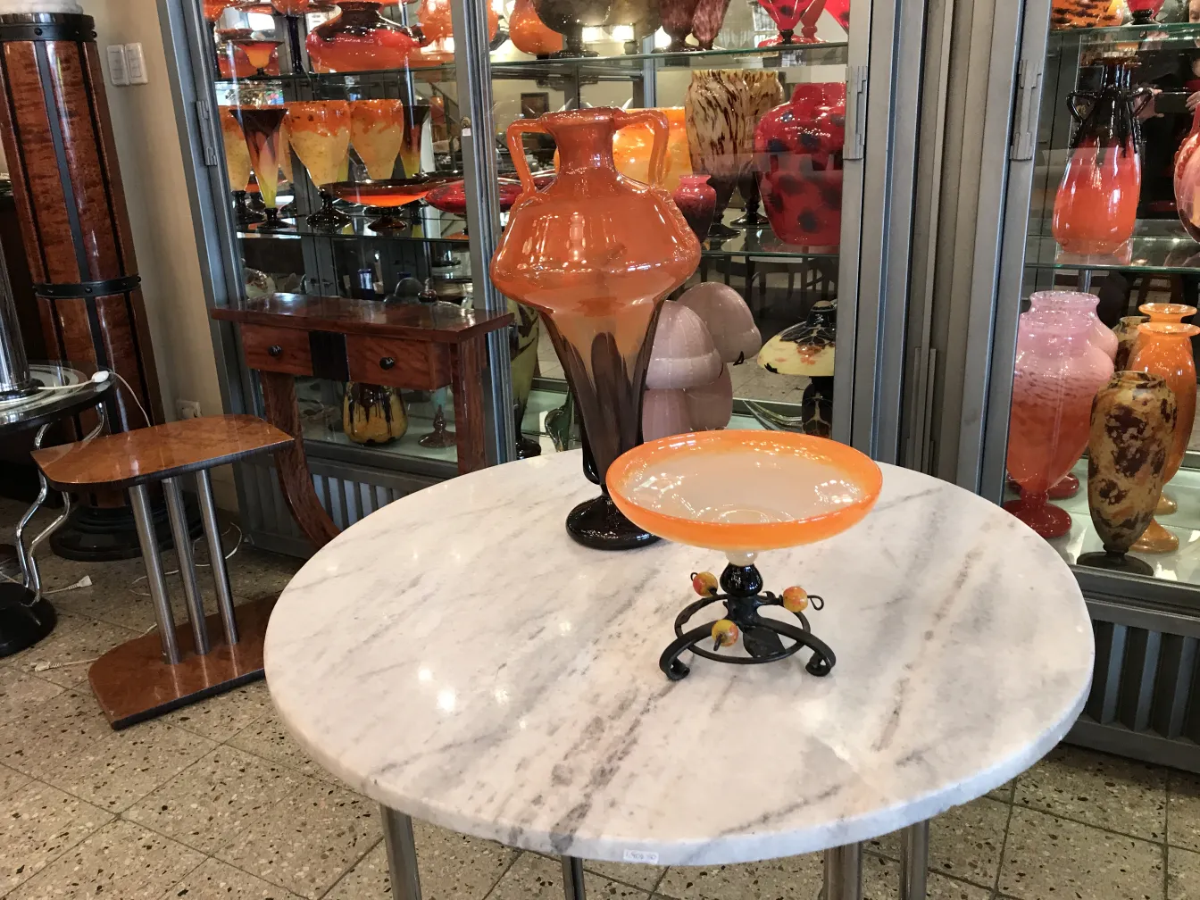 Verre signé Schneider exposé parmi des objets colorés d'antiquités.