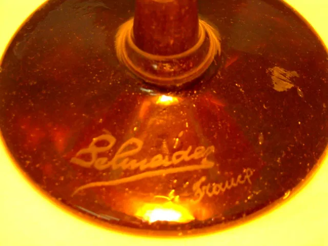 Verre signé ancien de Schneider avec détails visibles. Ambiance sophistiquée.