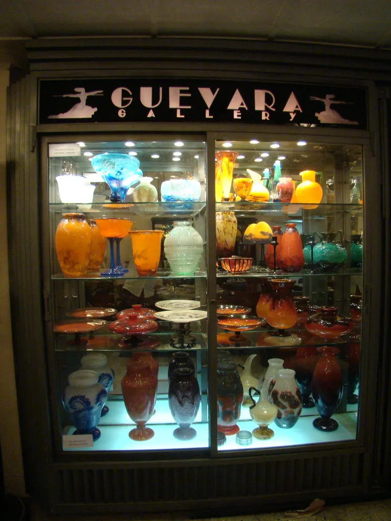 Exposition d'antiquités avec verre signé de Schneider, vases colorés en vitrine.