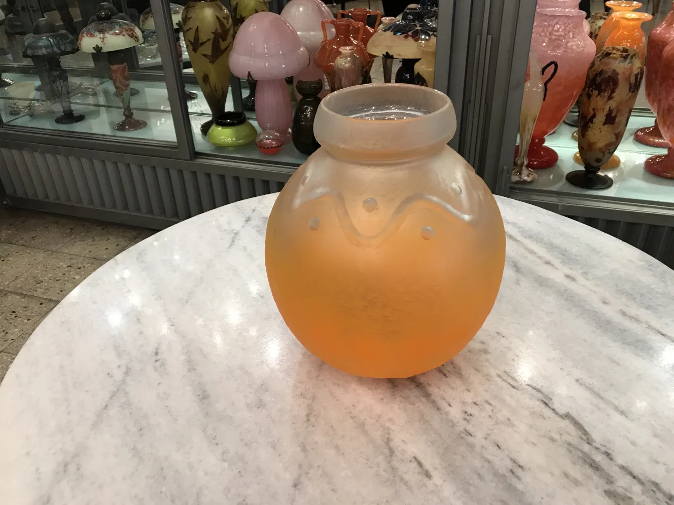 jarrón de vidrio naranja mate, con toques decorativos, exhibido entre antigüedades coloridas