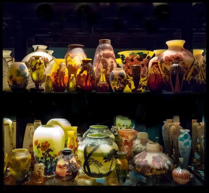 Collection of glass vases signed by Schneider with various colors displayed on shelves
