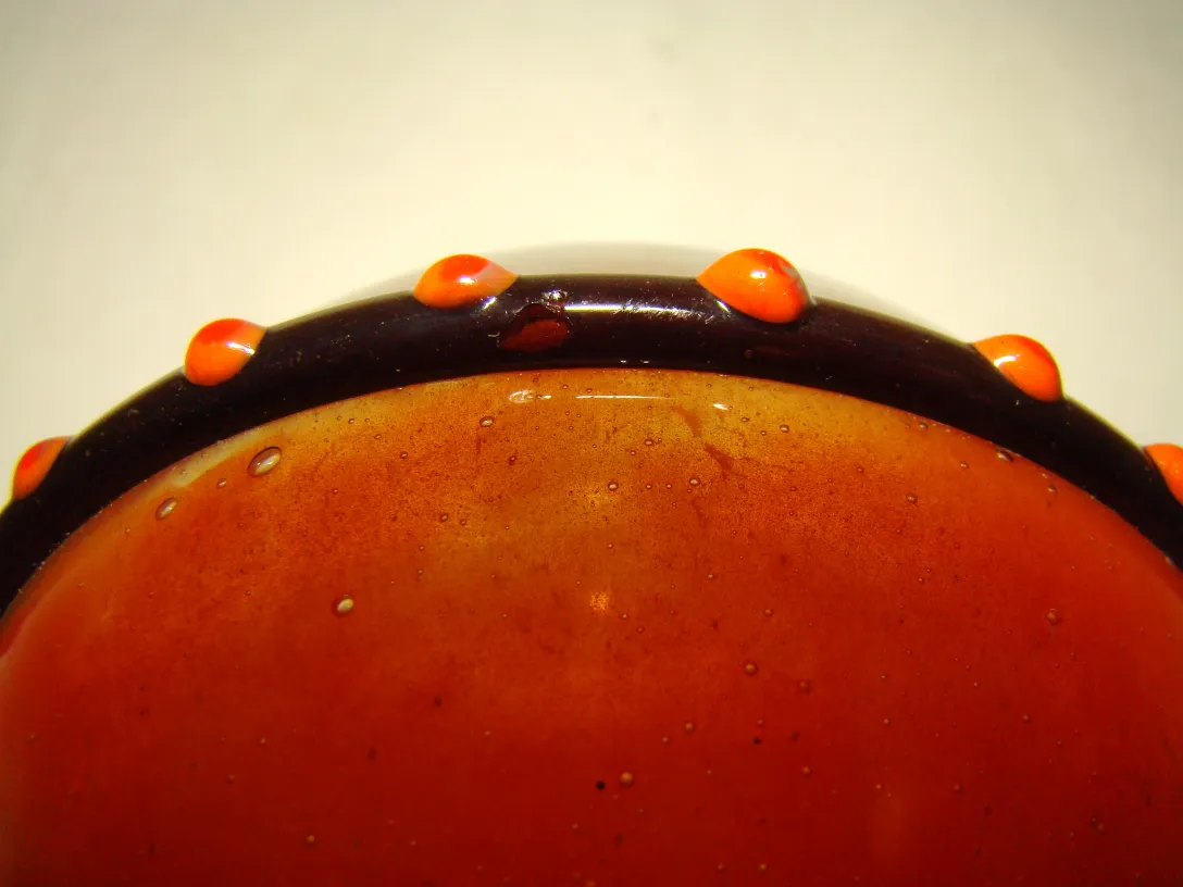 detail of an antique signed glass schneider in amber color with decorative edges