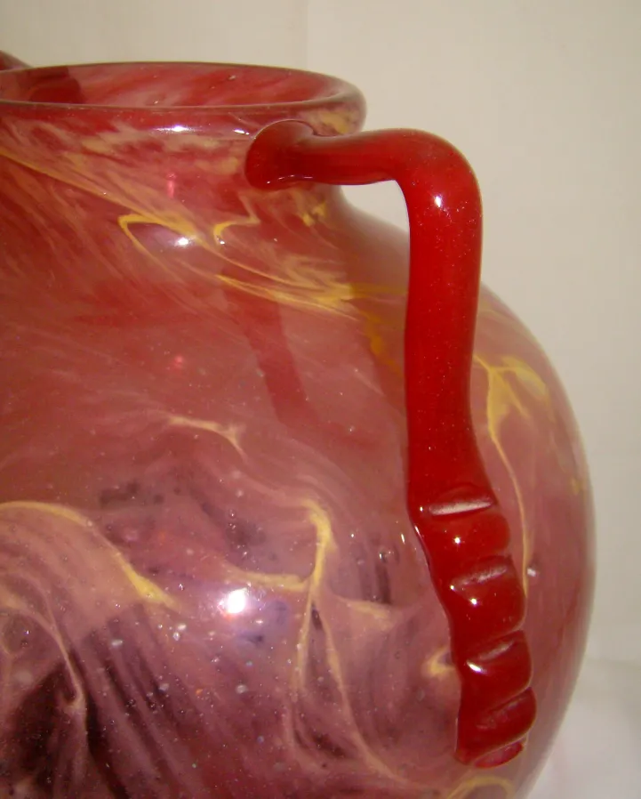 jarra de vidrio antiguo con un diseño de colores mezclados y un asa roja.