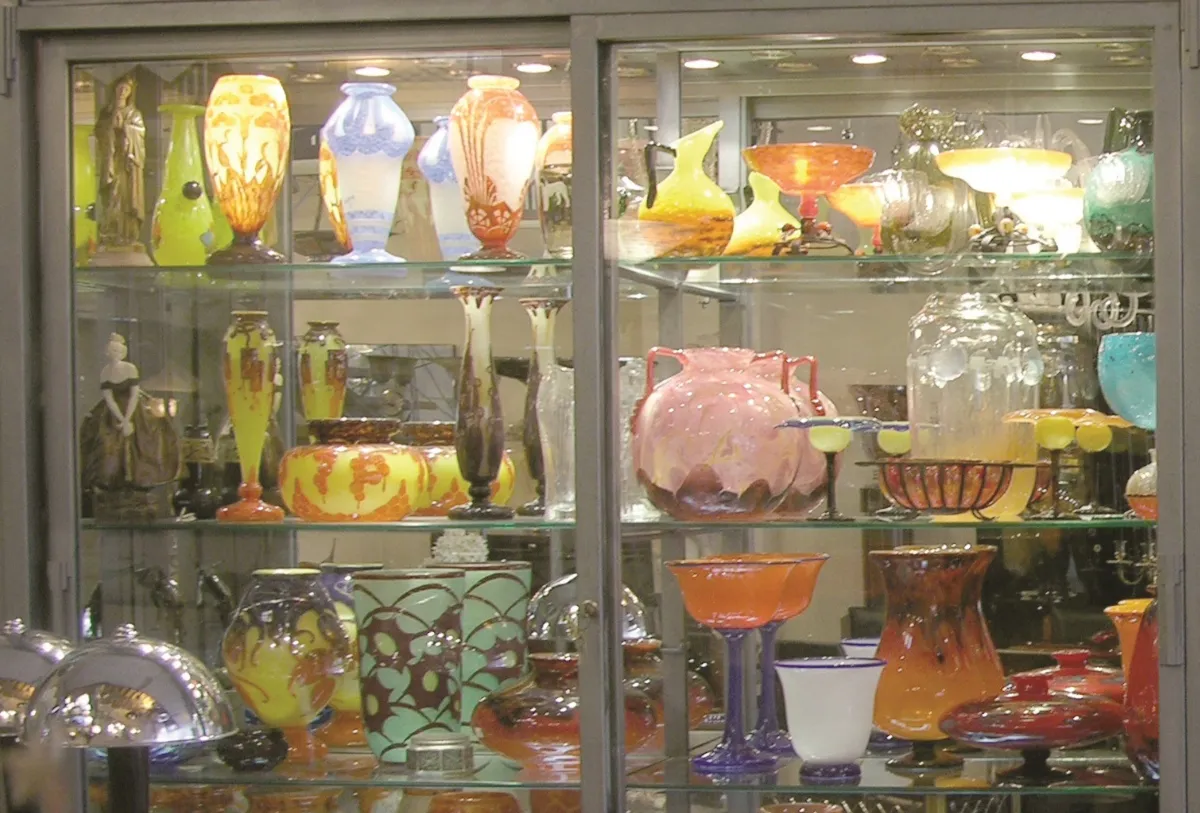 Vetrina con antiquariato in vetro firmato Schneider, che presenta vari colori e forme.