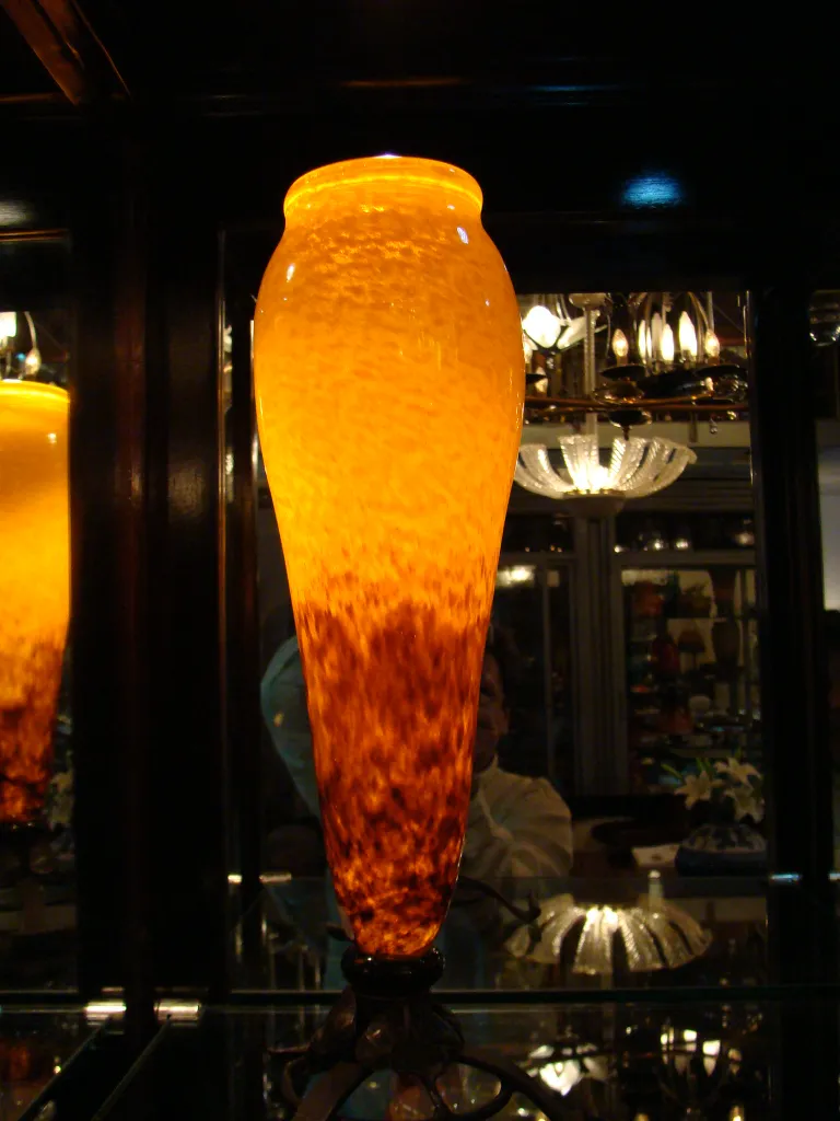 Vaso de vidro assinado Schneider em cor âmbar com design único, ambientado em uma vitrine.