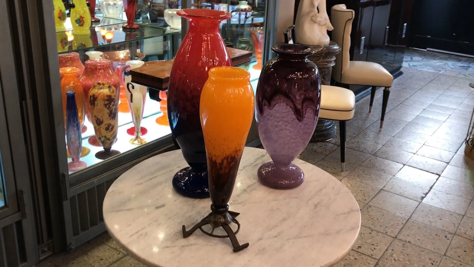 Trois vases en verre signés Schneider, colorés et décoratifs, exposés dans une vitrine.