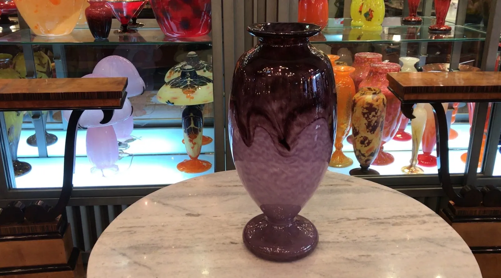 Vase aus signiertem Glas von Schneider in lila Tönen, umgeben von bunten Antiquitäten.
