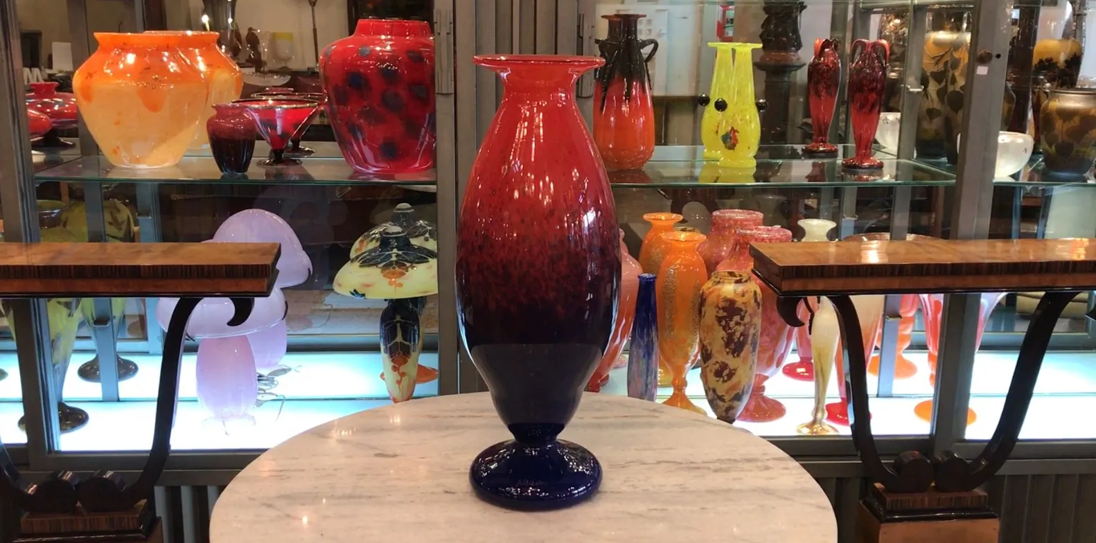 Verre signé Schneider aux teintes rouges et bleues, entouré d'antiquités.