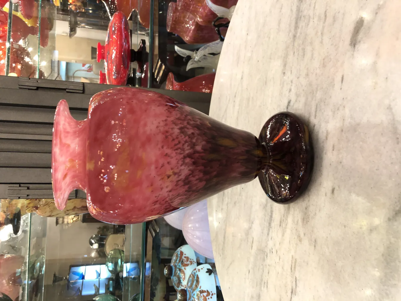 Antigo vaso de vidro assinado por Schneider em cor rosa com base escura em um ambiente de antiguidades.