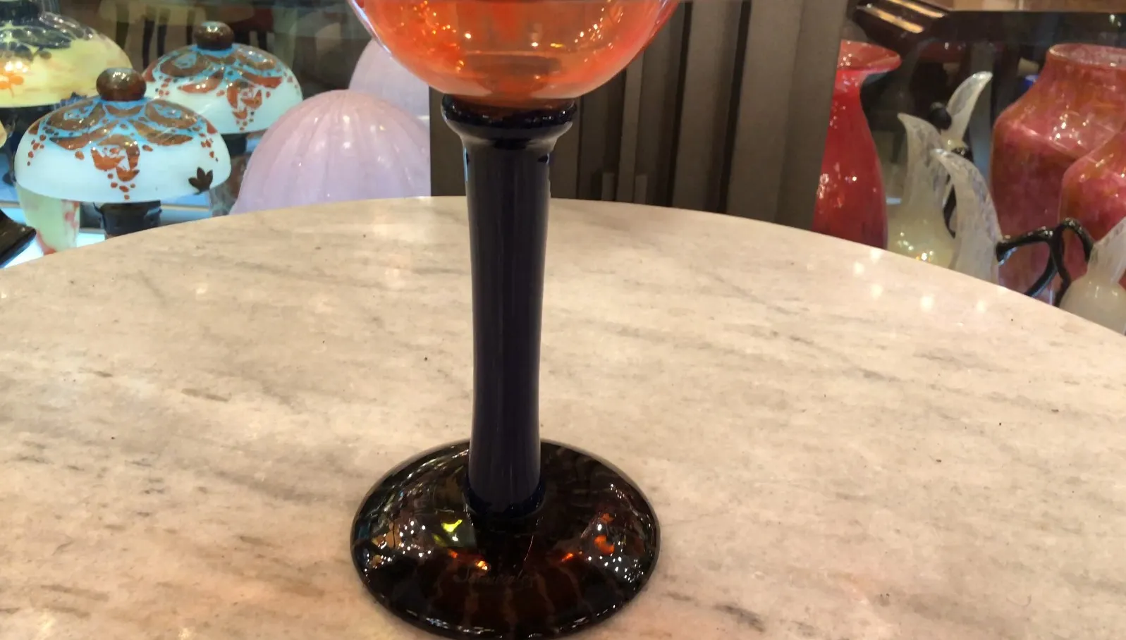 orangenes signiertes Glas mit dunklem Fuß