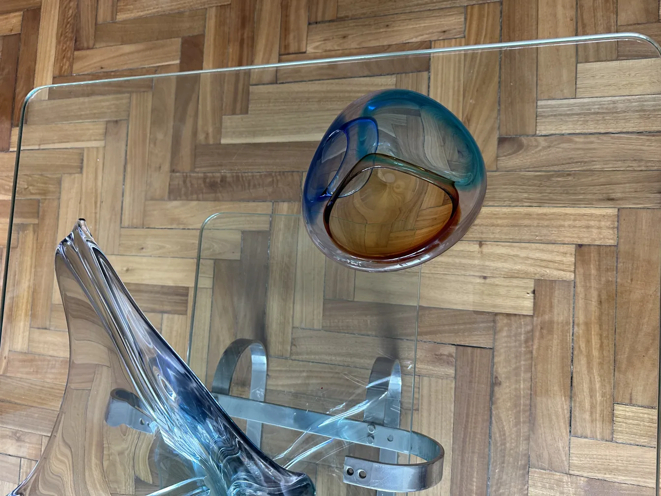 murano-glas-stück in blau-braunen farbtönen, sanfte formen, auf einem glastisch