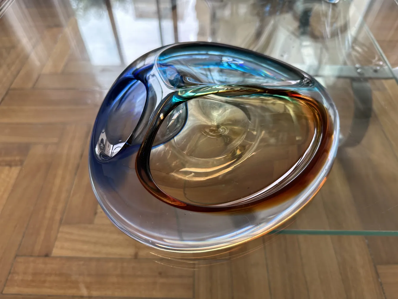 Hermoso cristal de murano con tonos azules y ámbar, sobre mesa de madera.