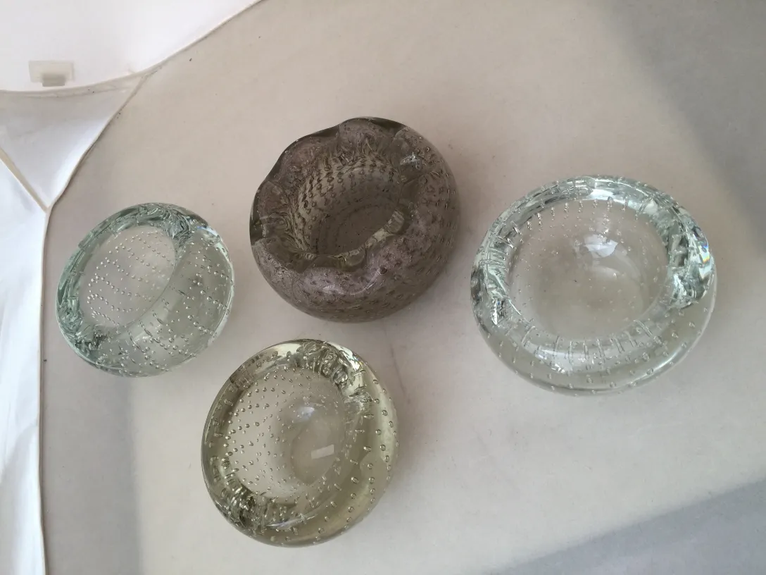 quatre pièces de cristal de murano de différentes couleurs et formes, sur un fond clair.