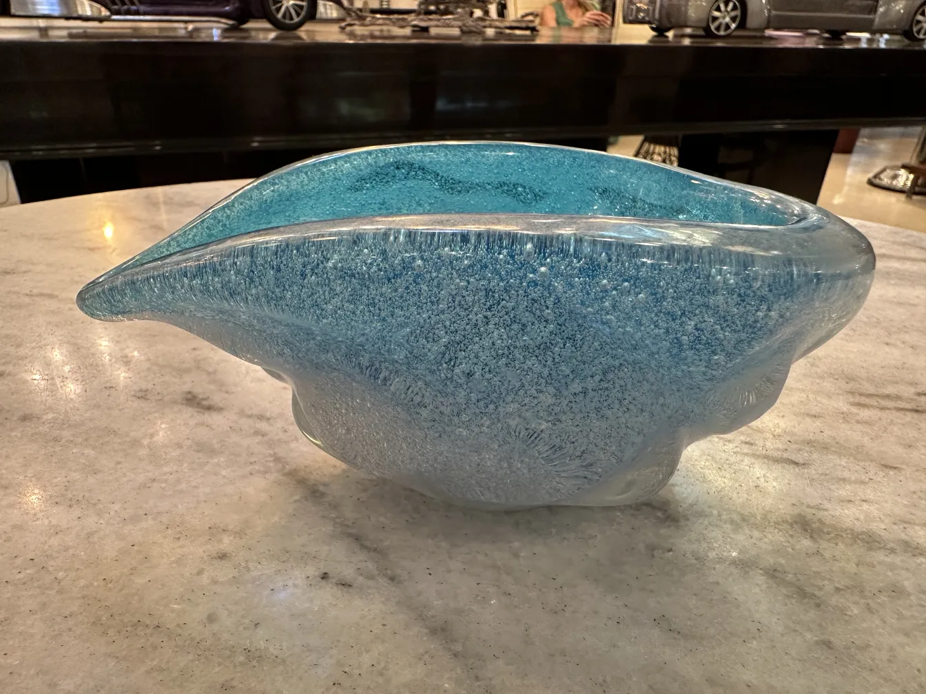 Un elegante antico vetro di murano in tonalità blu, con forma organica, su un tavolo in marmo.