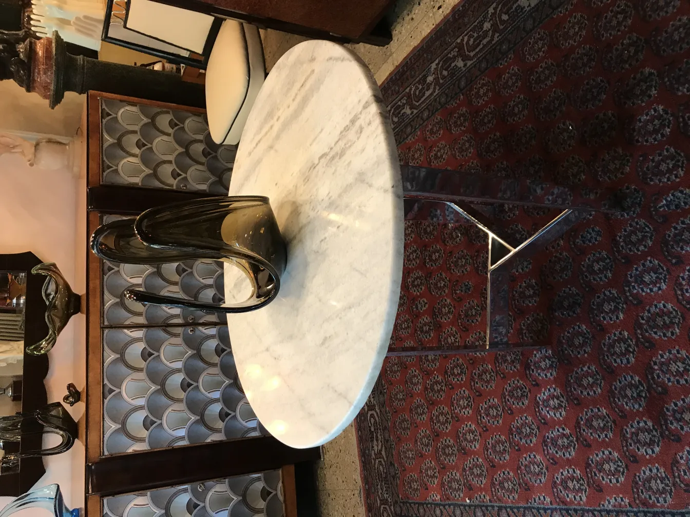 Elegante jarrón de cristal de Murano en forma fluida sobre mesa blanca, fondo con sillones antiguos