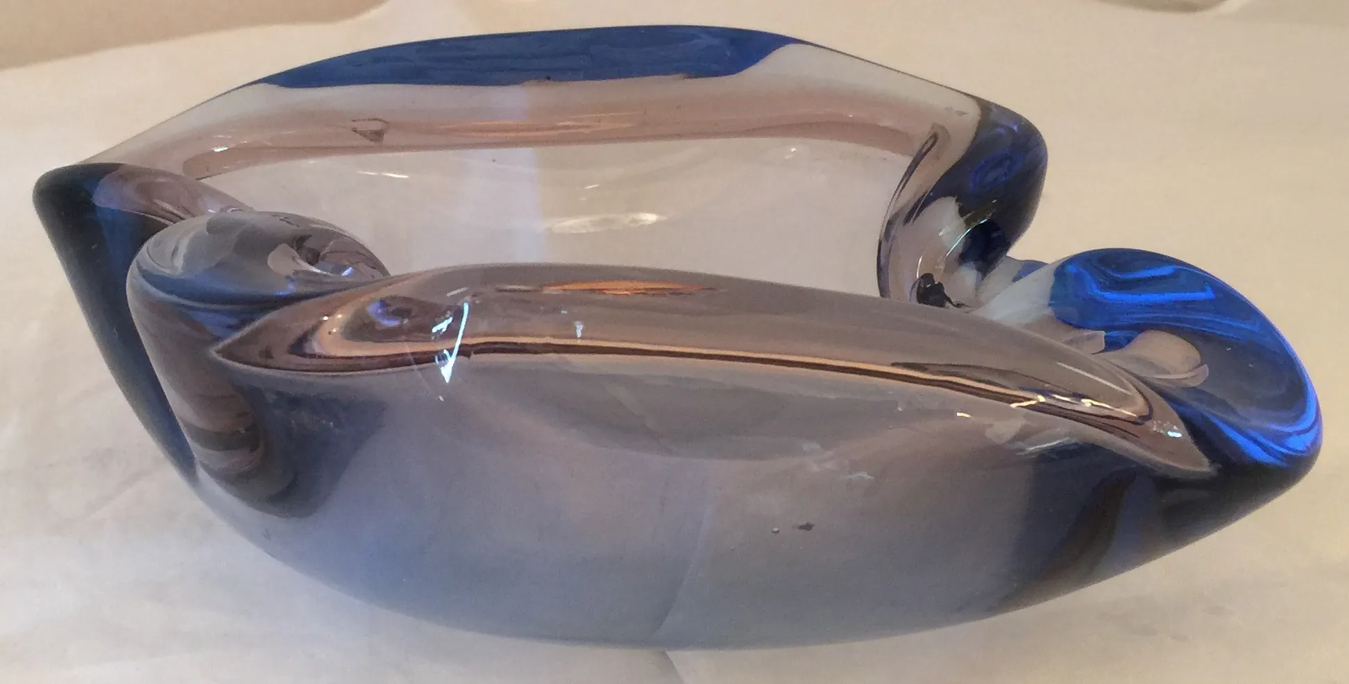 peca de cristal de murano em tons azuis e transparentes, forma estilizada contra um fundo claro