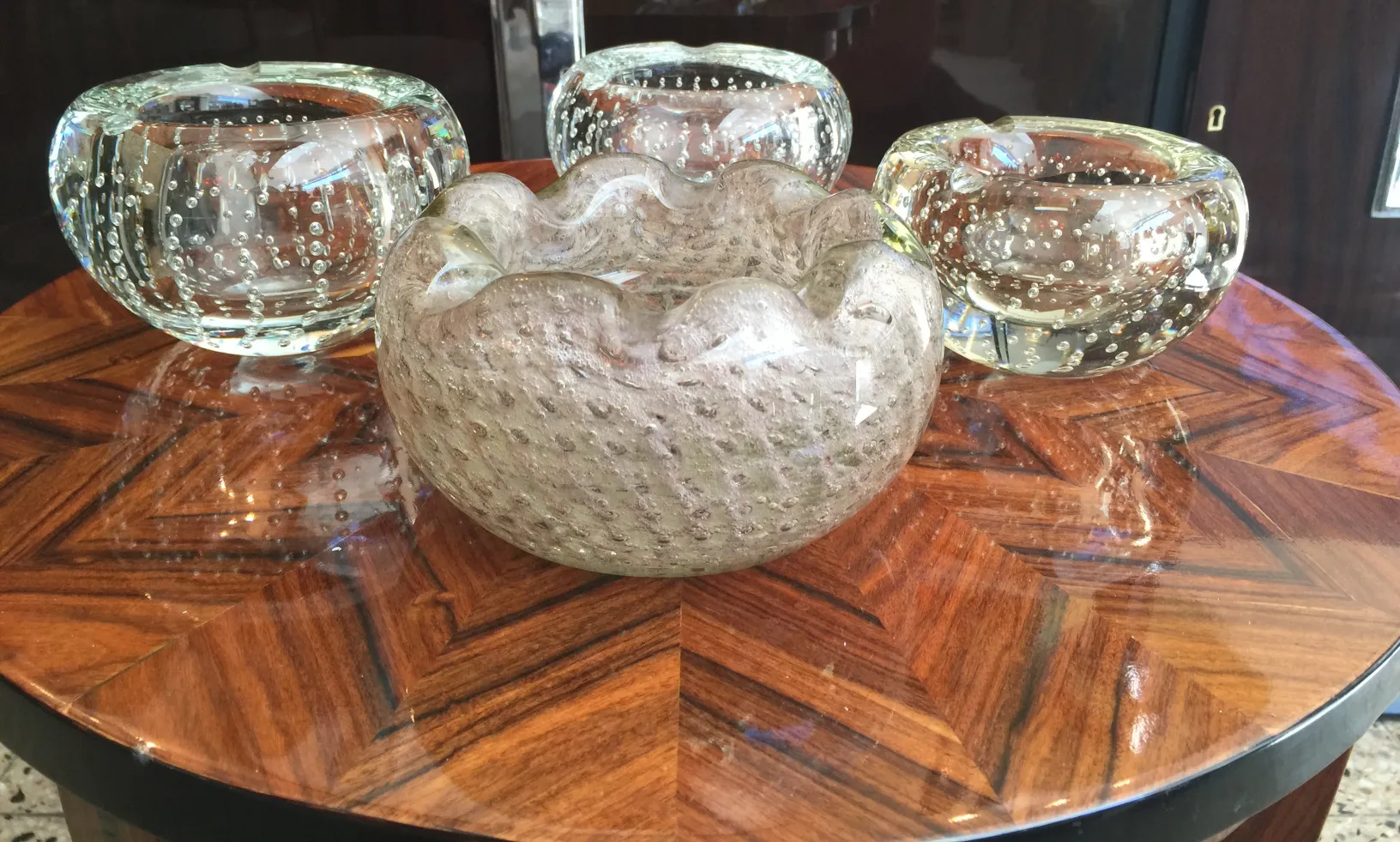 Cristal de Murano en tonos suaves, con burbujas decorativas, tres piezas distintas sobre una mesa elegante.