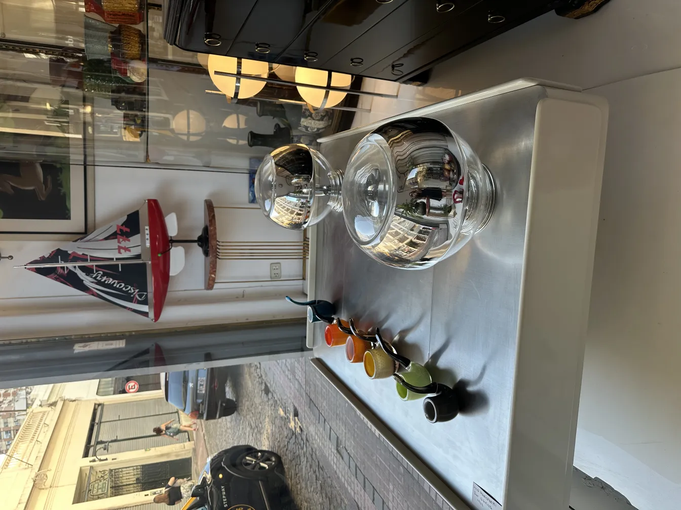 Cristal de Murano antigo em uma vitrine com itens coloridos e um veleiro decorativo ao fundo.