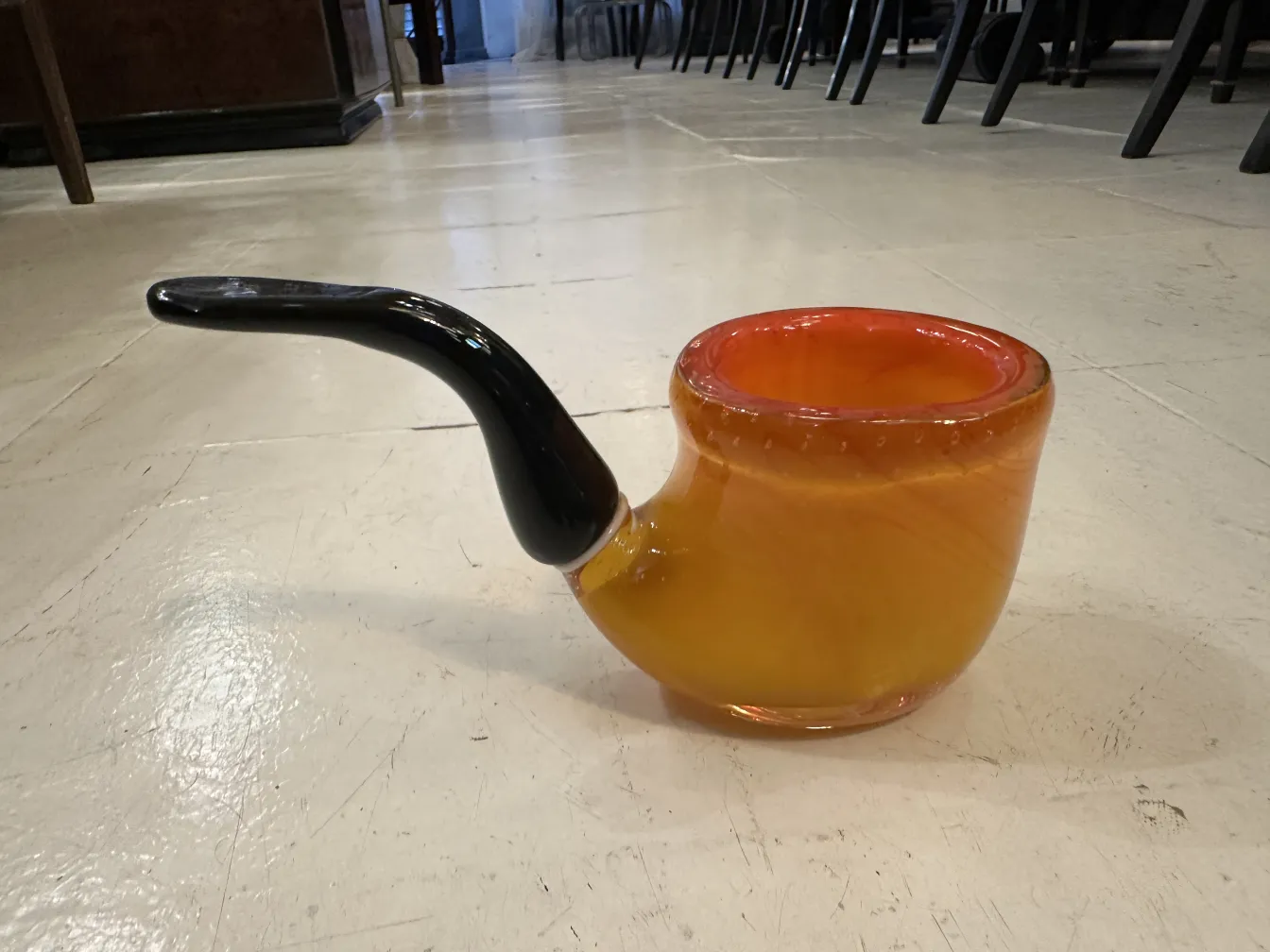 Antigo cristal de Murano decorativo em tons de laranja e preto, com design elegante, cercado por cadeiras que adicionam contexto.