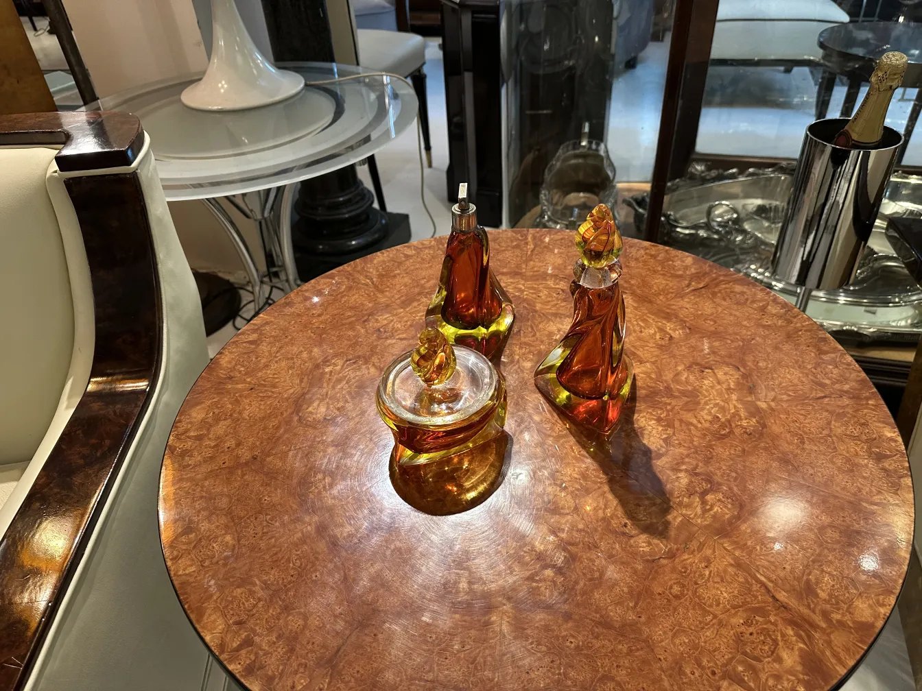 Tre pezzi antichi di vetro di Murano in tonalità ambrate su un tavolo di legno.