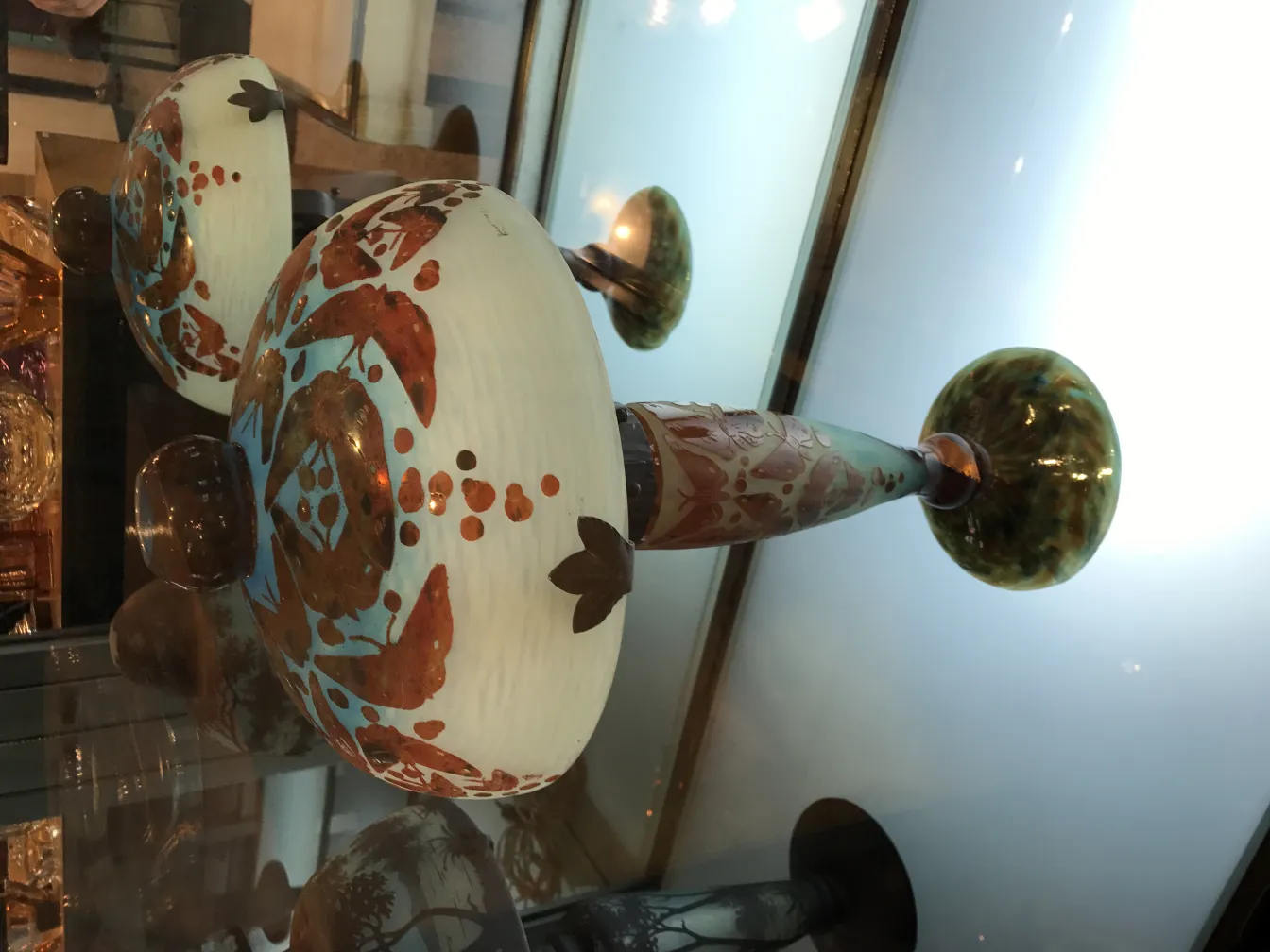 Antigua pieza de vidrio con detalles decorativos y firma, reflejando colores vibrantes, exhibida en un entorno elegante.