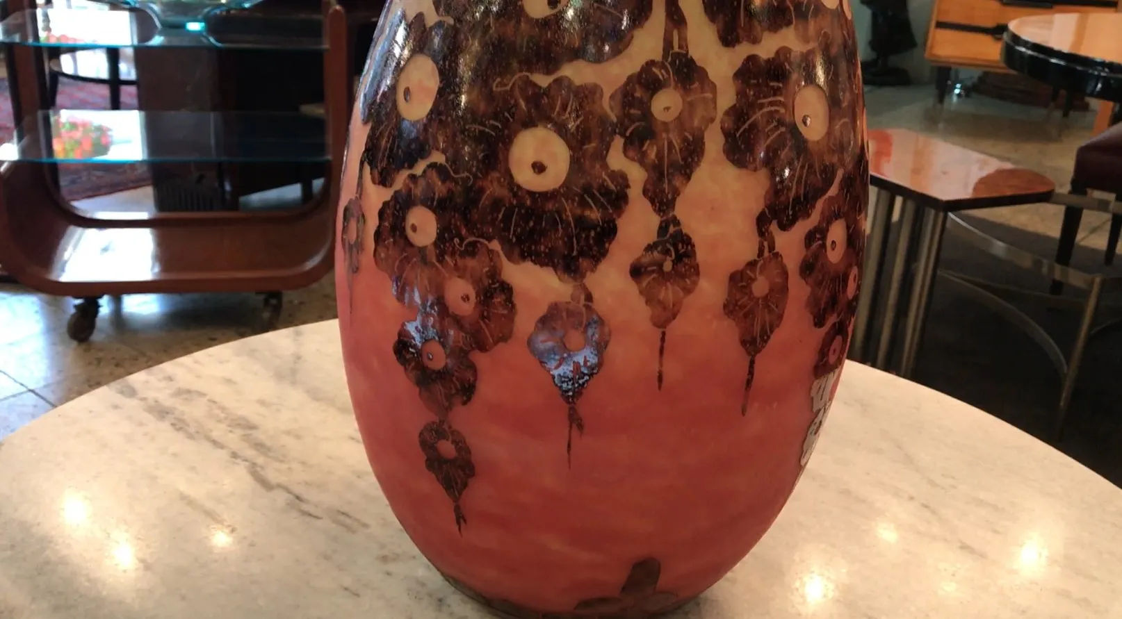 Antike Glasvase mit Signatur Le Verre, mit schwarzen Blumenmotiven auf rotem Hintergrund. Antike Möbel im Hintergrund.