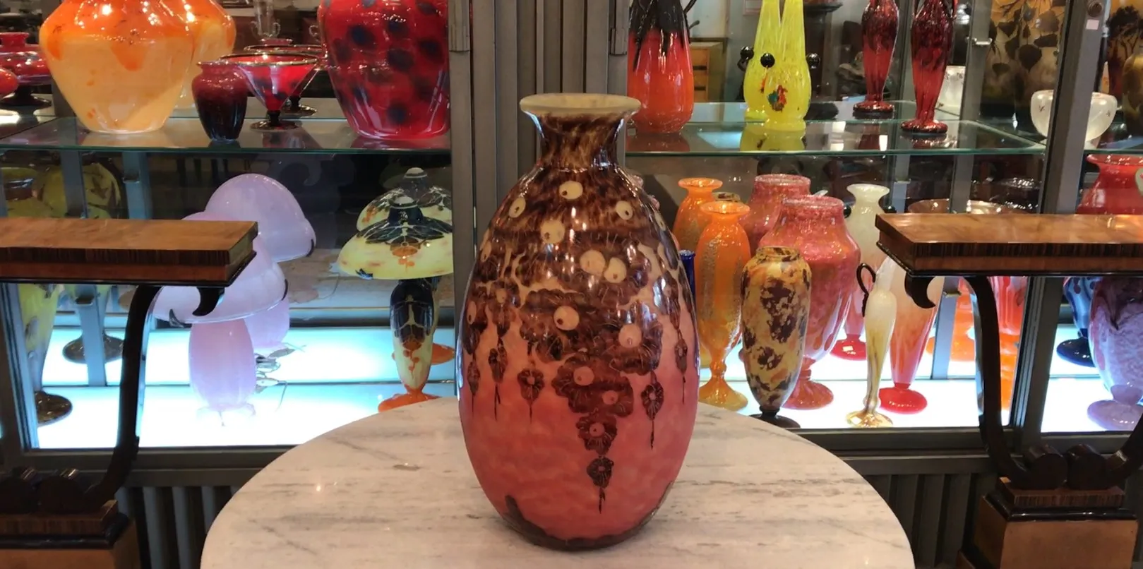 Vaso in vetro antico firmato con tonalità rosa e marrone in un ambiente di antiquariato.
