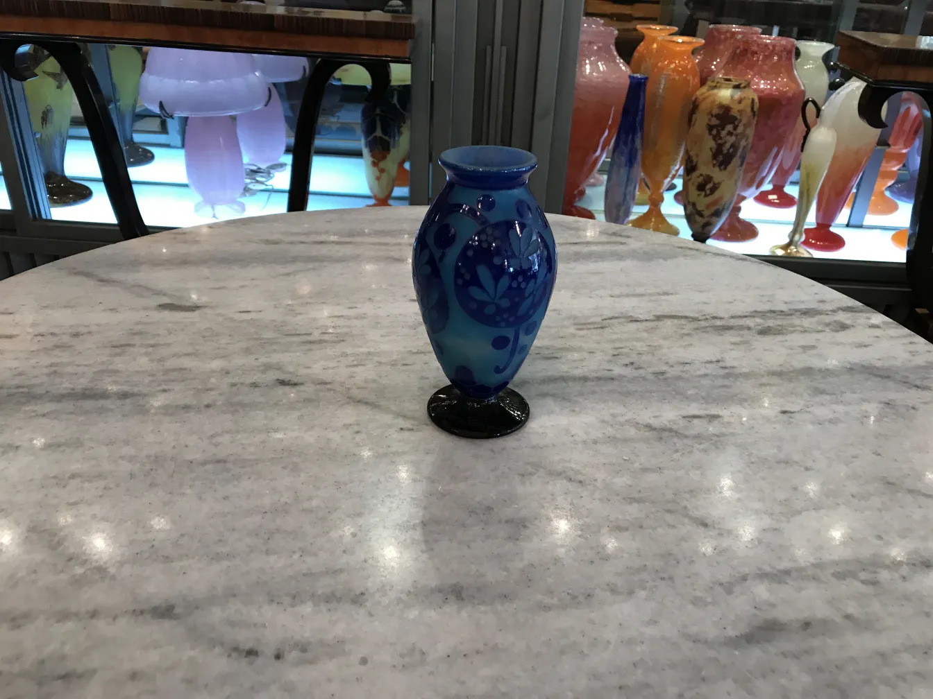 Decorativo vidrio azul firmado con detalles florales en un fondo de antigüedades.