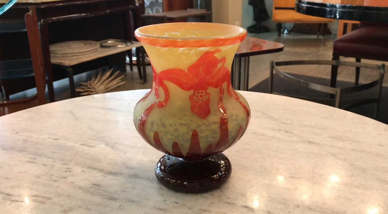 Vase ancien en verre signé Le Verre avec un design de fleur en jaune et rouge, posé sur une base sombre.