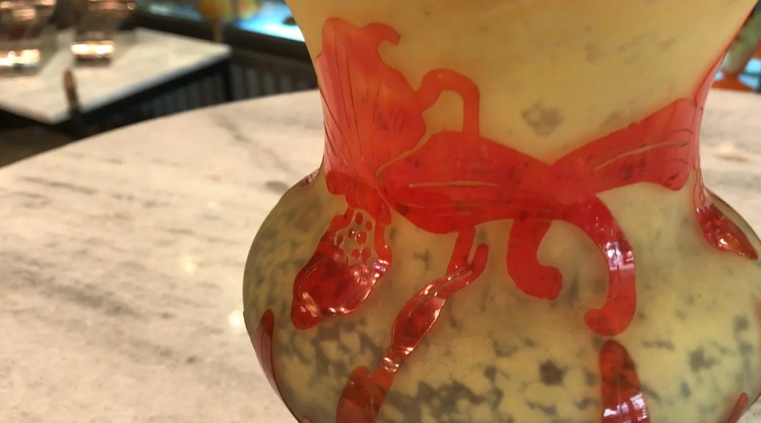 Vidro assinado Le Verre com detalhes decorativos vermelhos e fundo claro, apresentado sobre uma mesa.