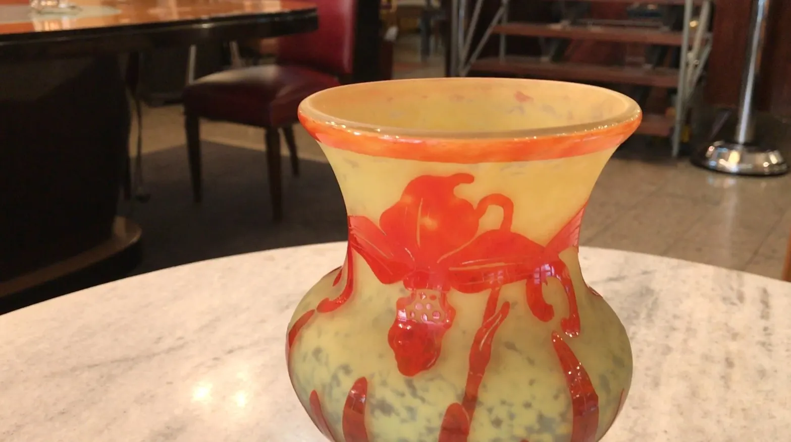 Vaso decorativo antigo, vidro assinado Le Verre, com detalhes em vermelho e amarelo em um ambiente de restaurante